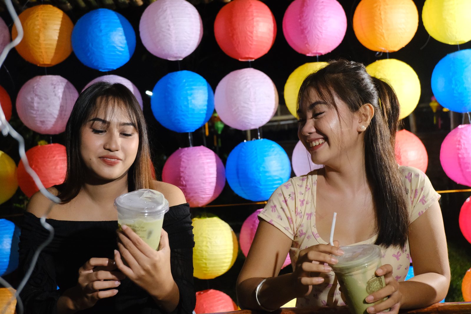 Two friends laughing under strings of paper lanterns at night